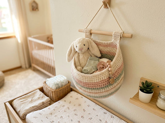 Pastel crochet nursery wall basket holding baby items and a plush toy