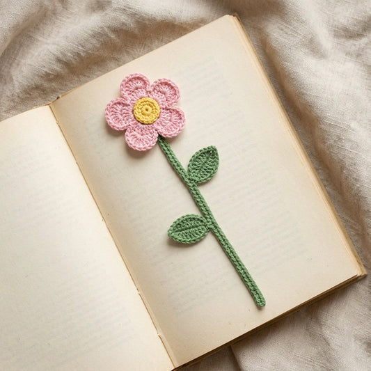 Crochet flower bookmark with pink petals and yellow center resting diagonally across an open book