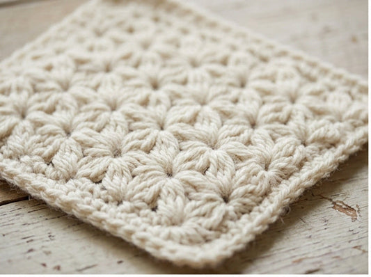 Close-up of cream jasmine stitch crochet fabric with dense floral puff stitch texture