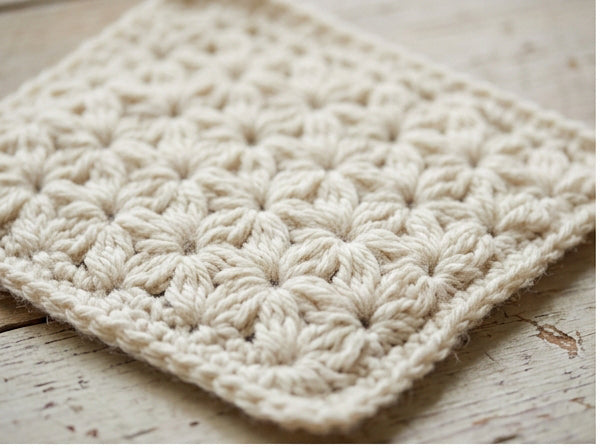 Close-up of cream jasmine stitch crochet fabric with dense floral puff stitch texture